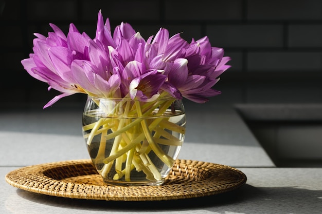 Purple crocus flowers in a glass vase standing on a woven mat